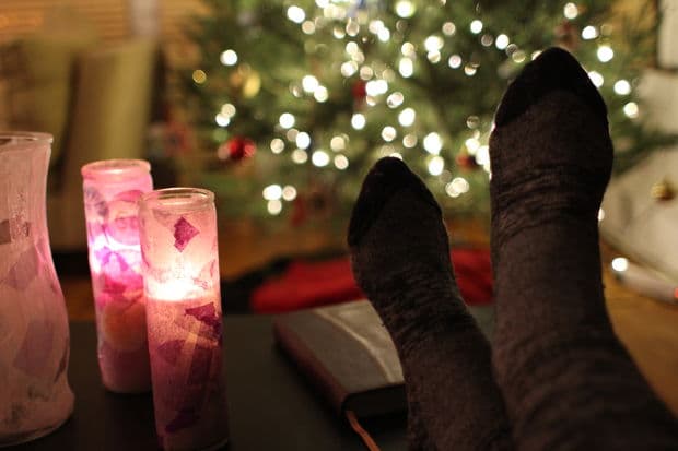 Feet in cozy socks near lit candles, with a blurred Christmas tree in the background.