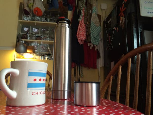 Coffee mug, metal thermos, and lid on a red polka-dot table in a cozy kitchen.
