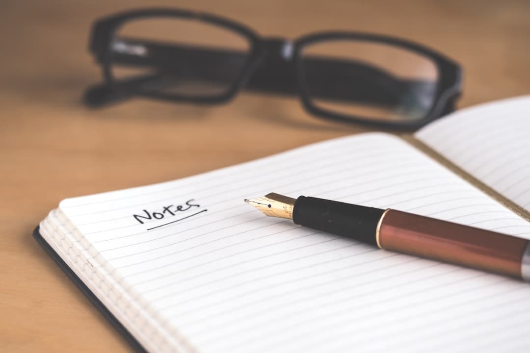 Fountain pen on an open notebook with "Notes" written, glasses in the background.