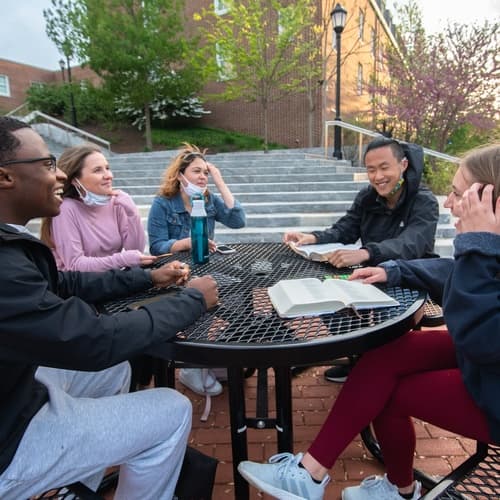A group of students sitting outside around a table smiling.