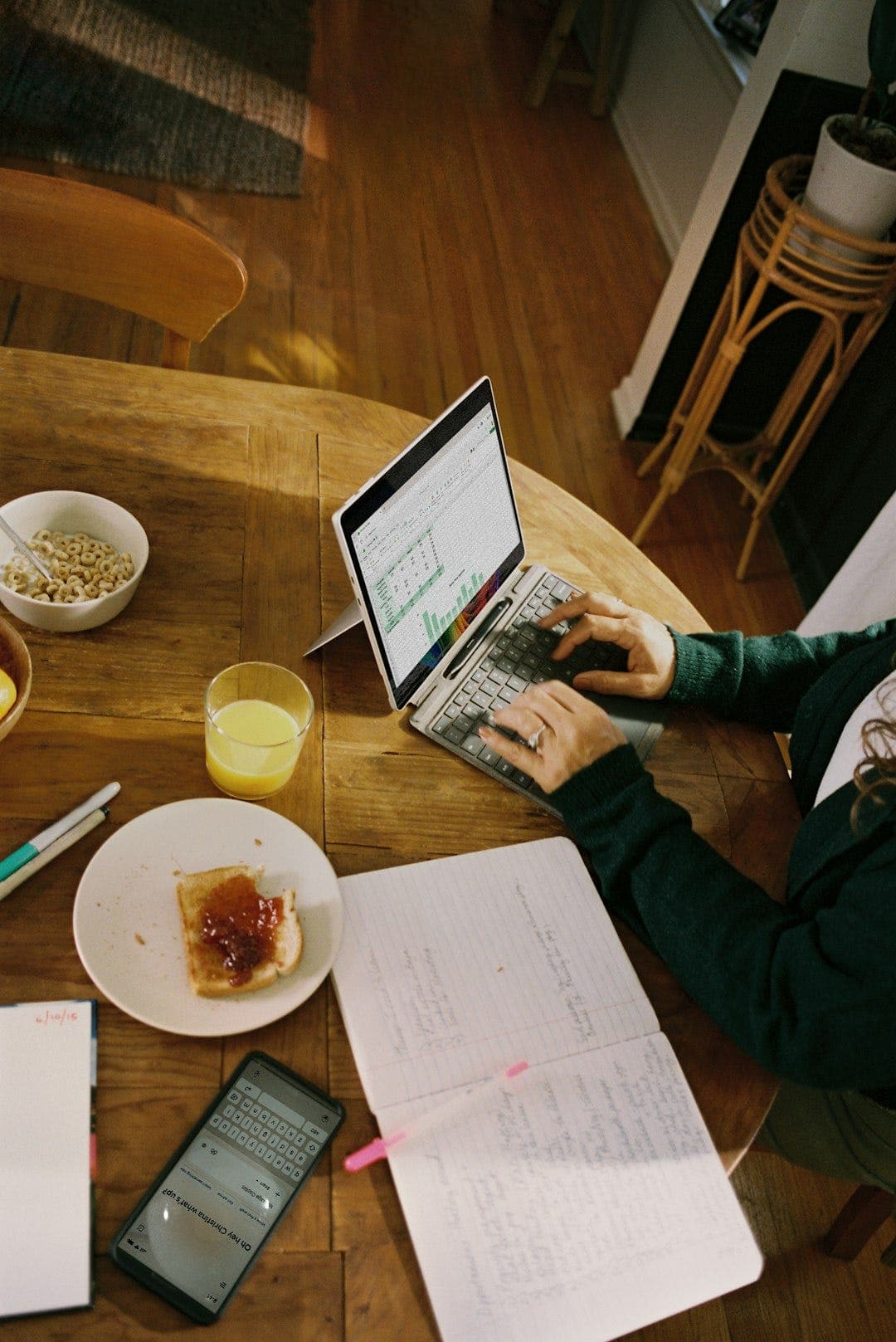 A person works on a laptop beside a notebook and coffee.