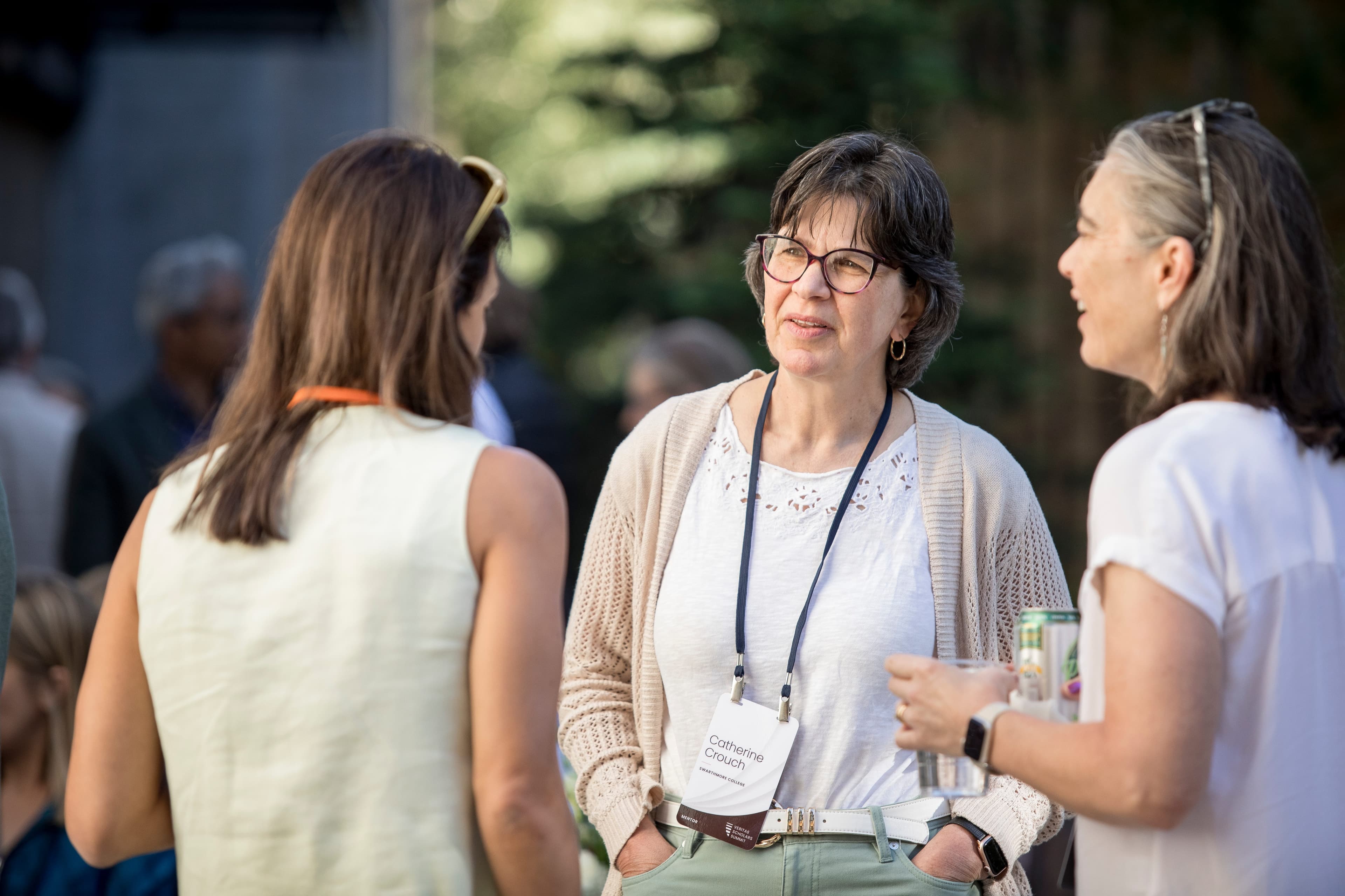 Three women wearing name badges talk outdoors.