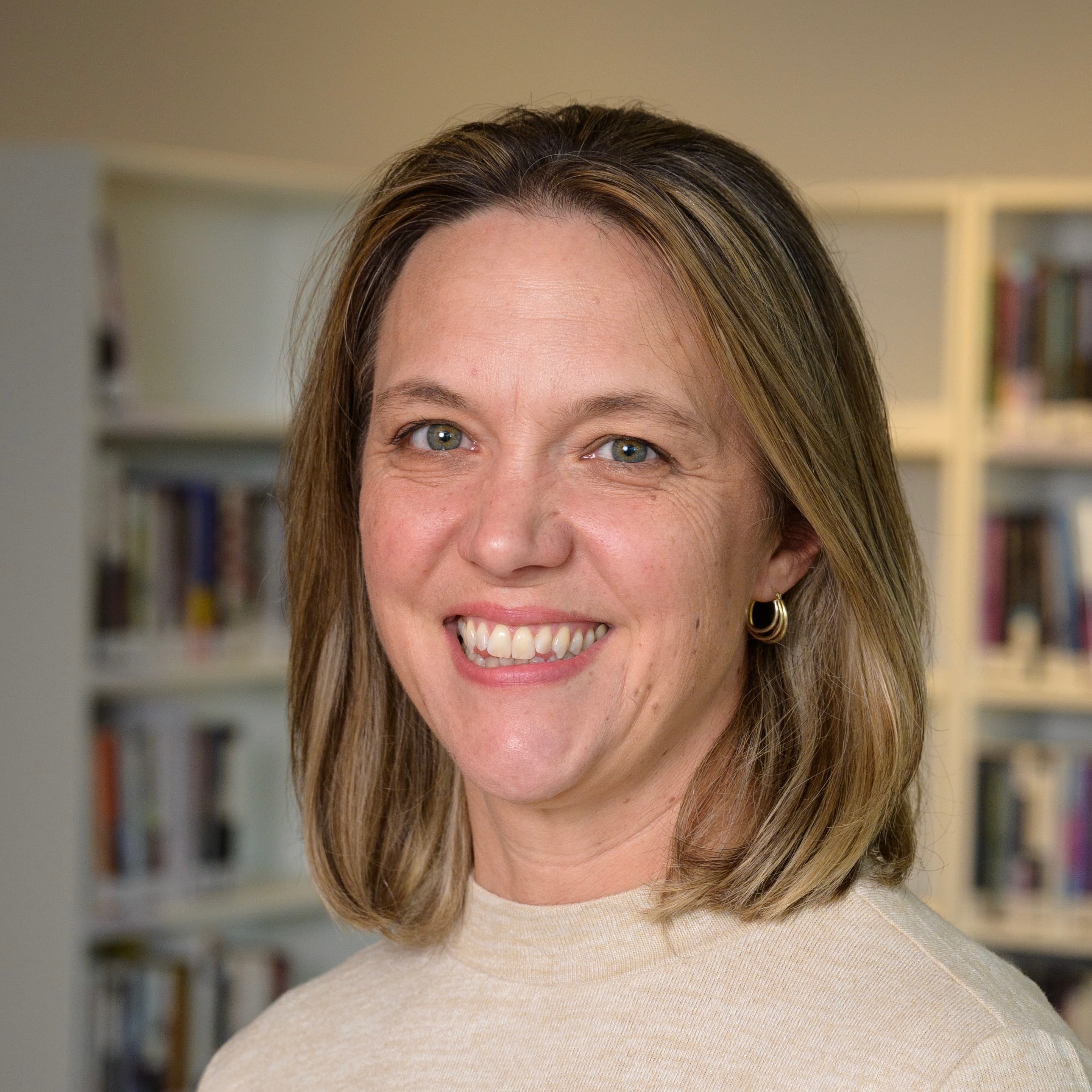 Portrait of a smiling woman with shoulder-length hair in front of bookshelves.