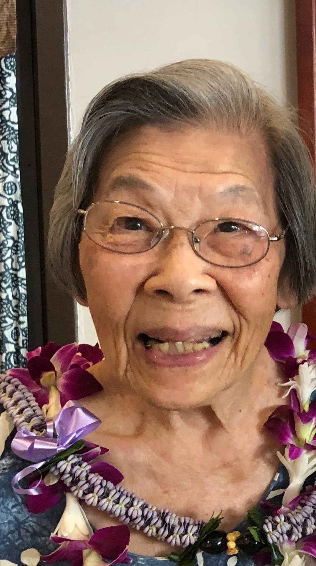 A smiling woman wearing glasses and flower leis in a doorway.